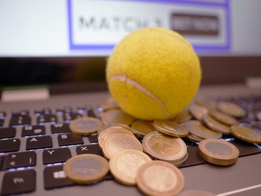 imagen en la que aparece una pelota de tenis y unas moedas de euro sobre un teclado de un ordenador