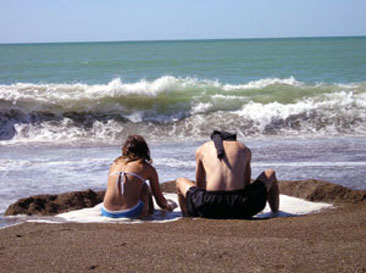 ideas para bañadores 2022. Pareja de hombre y mujer sentados en la playa