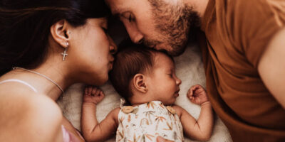 Fotografía de portada sobre el artículo de fotografia newborn Barcelona en la que aparecen un bebé y sus padres rodeándolo en un ambiente acogedor