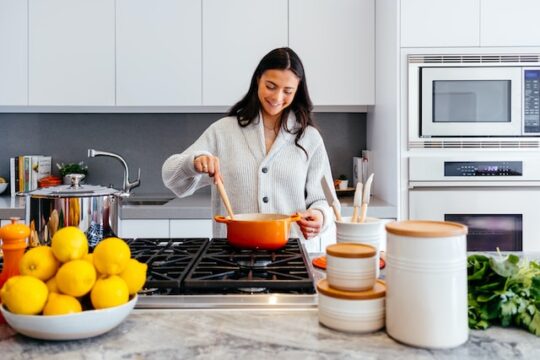 Imagen de una mujer cocinando con una cuchara de palo y una hoya de color anaranjado